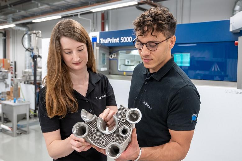 Two people hold an aerospace component made using additive manufacturing techniques.