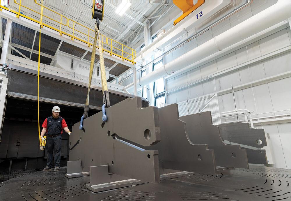 An AMADA employee guides part of a press brake that hangs from a crane.