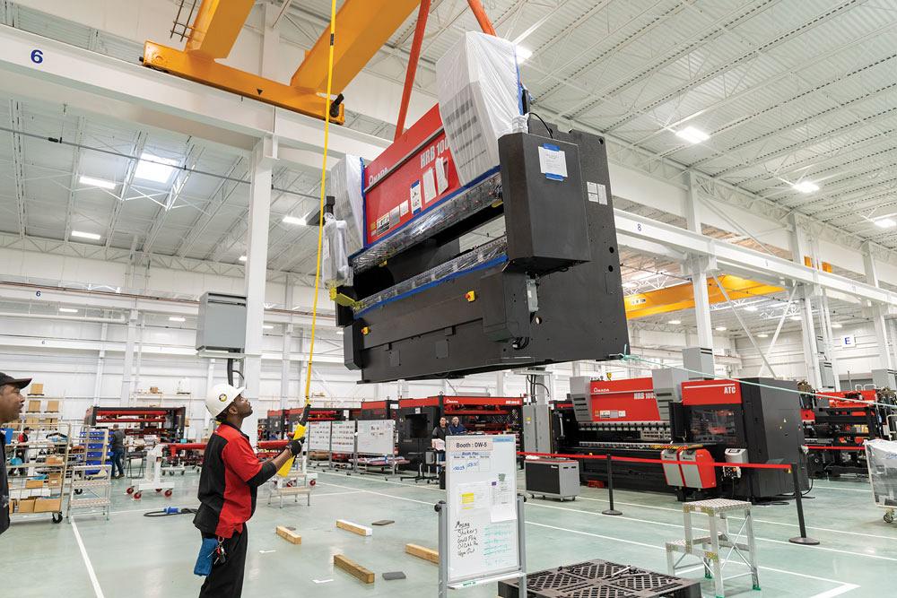 An AMADA employee moves a finished press brake into place using a crane.