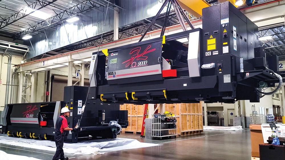A laser cutting machine is moved using a crane by an AMADA employee.
