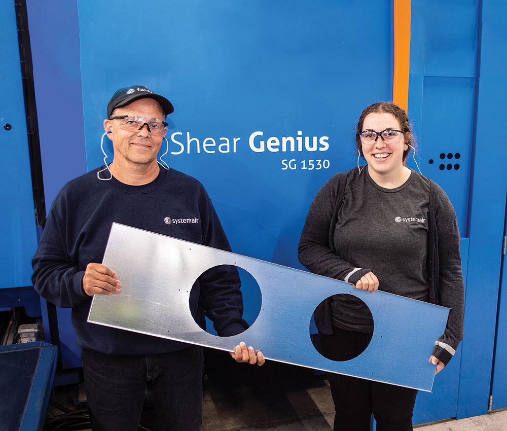 Employees Ron Gallant and Sylvie LeBlanc hold a part fabricated on the Shear Genius in front of the machine.