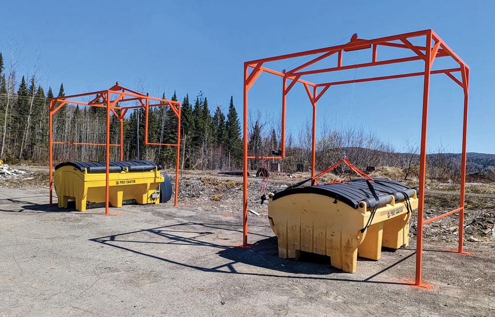 Two large containers are surrounded by metal frames used to lift the containers onto trucks. 