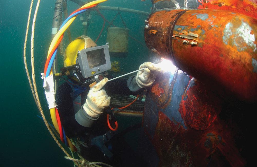Diver welds a repair patch on the submerged bow of a ship.