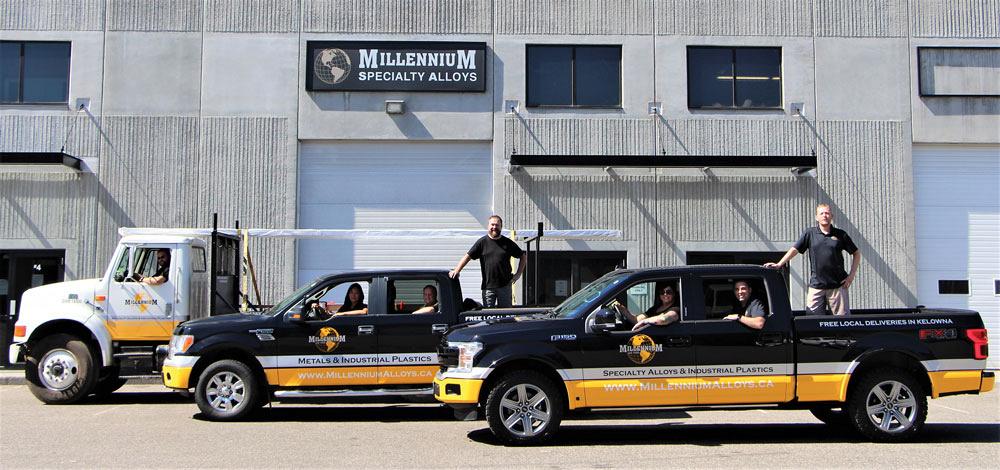 Three trucks stand in a line, emblazoned with the Millennium Specialty Alloys logo. Staff sit in the cab, while two more staff stand in the beds of two of the trucks. 