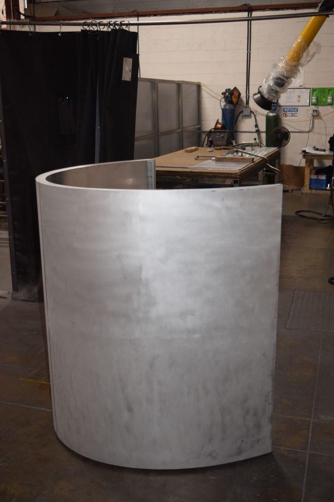 An arc-shaped column cover stands on a shop floor. 