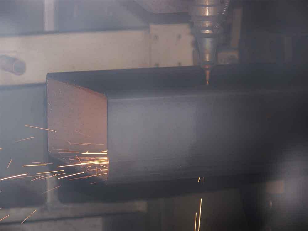 The 4-kW laser, viewed through the glass enclosure, cuts a section of square structural component.